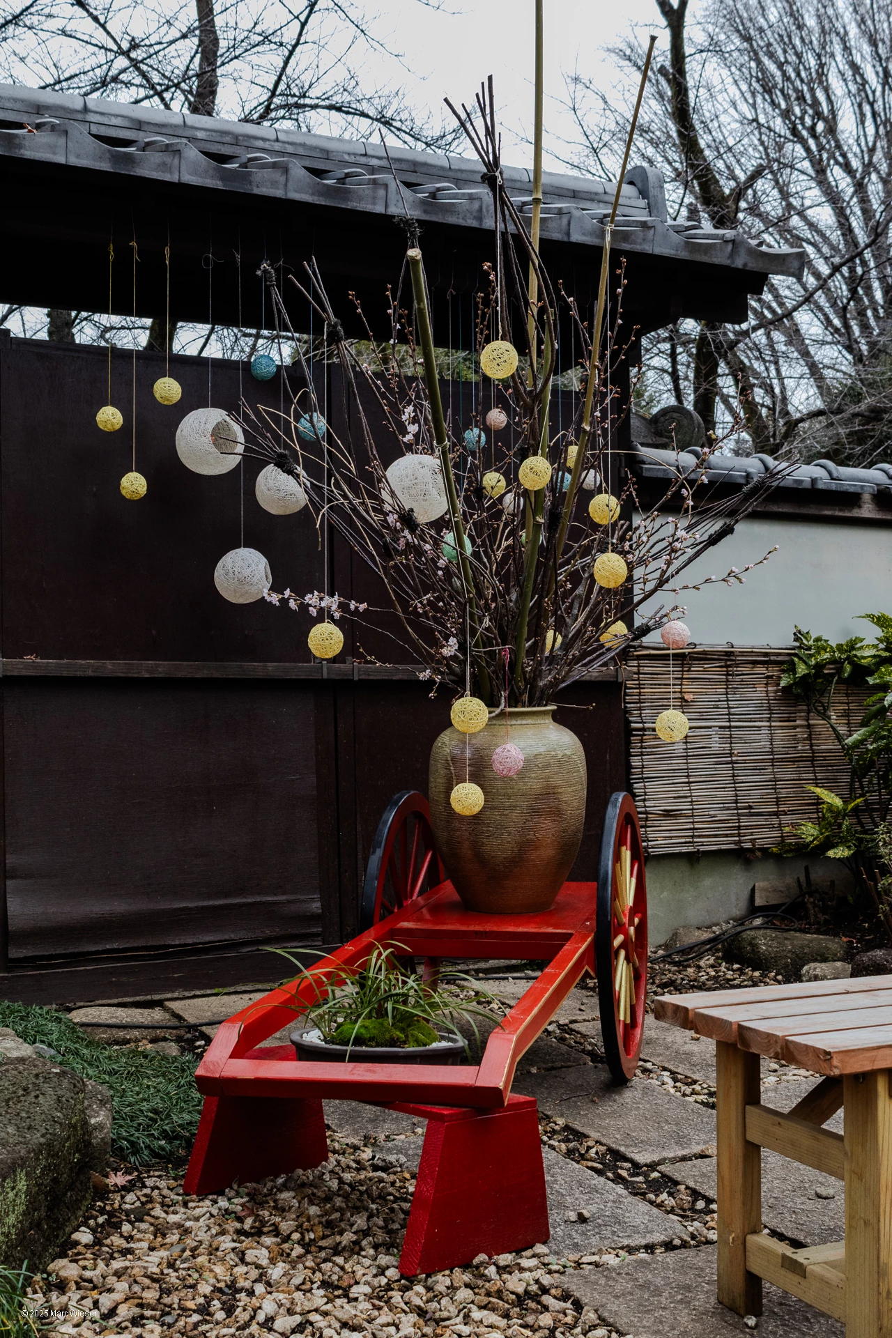 Photo verticale d’un arbre bourgeonnant dans un gros vase à taille humaine avec des boules décoratives suspendus à ses branches
