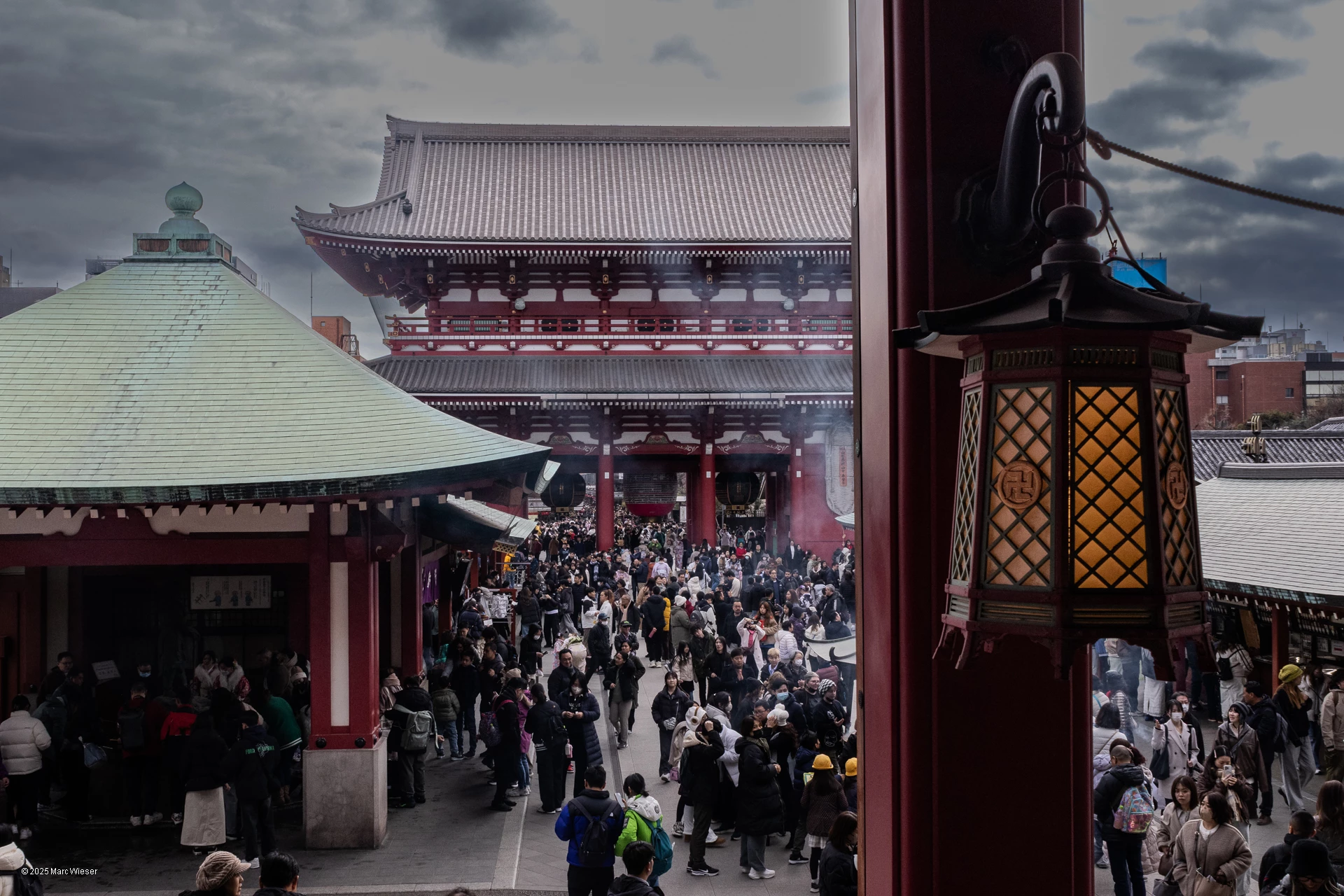Une lanterne accroché dans le temple Asakusa. La foule passant la porte du temple en fond dans les volutes de fumée d’encens