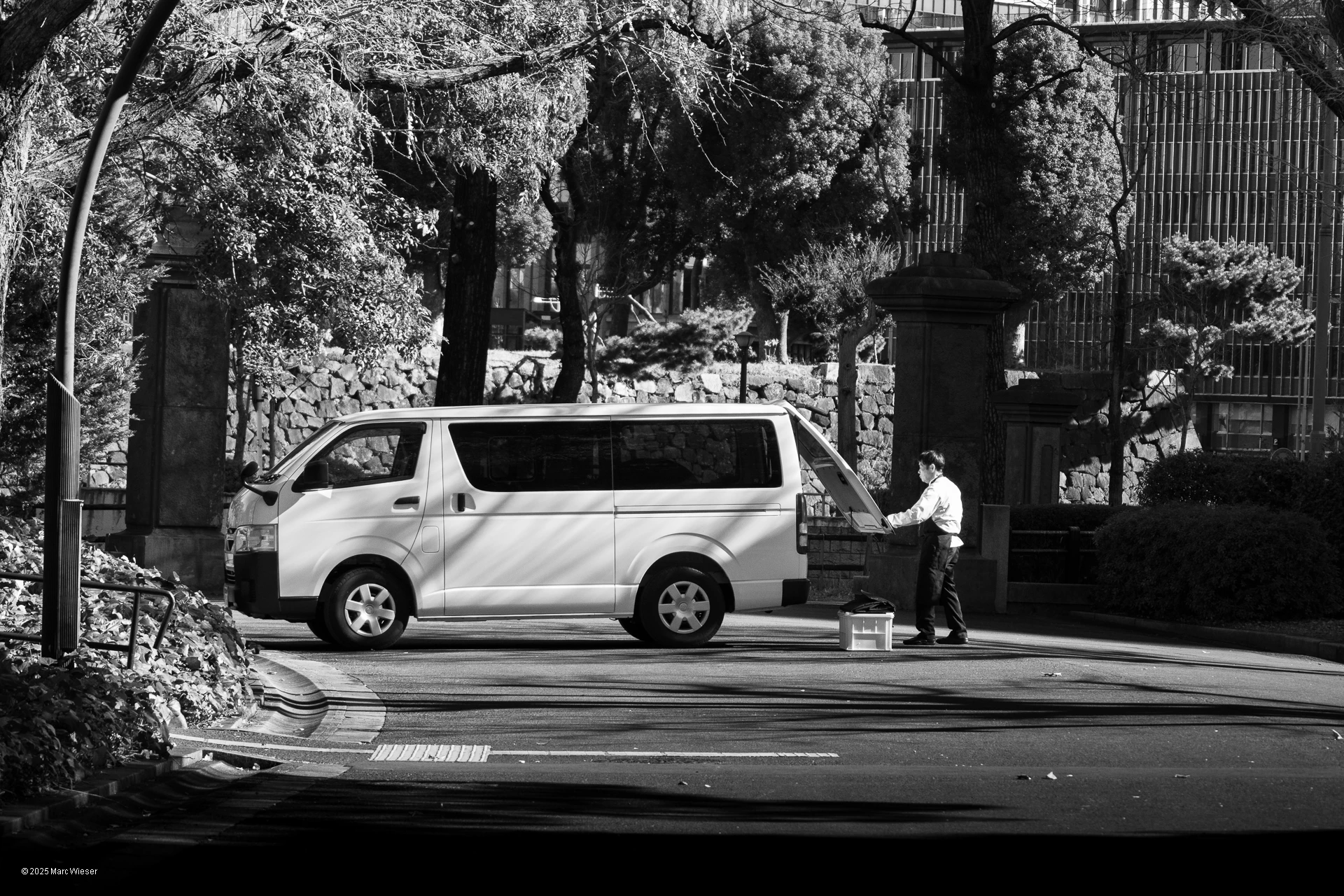 Photo en noir et blanc d’un travailleur ouvrant le coffre de son mini van